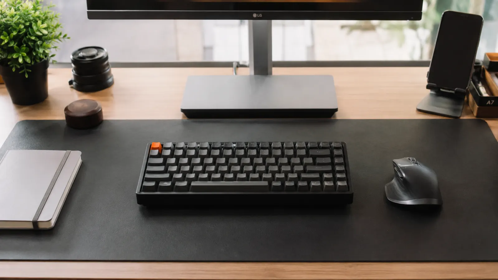 Organized home office desk with a leather desk pad anchoring keyboard, mouse, and phone stand in neat zones