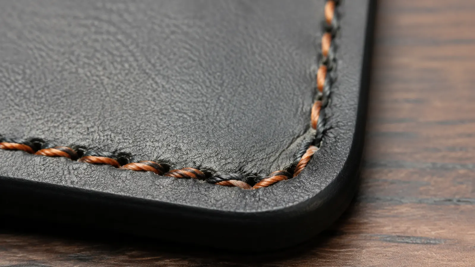 Close-up of the stitched edge of an Aothia desk pad showing the orange-brown contrast stitching along the border