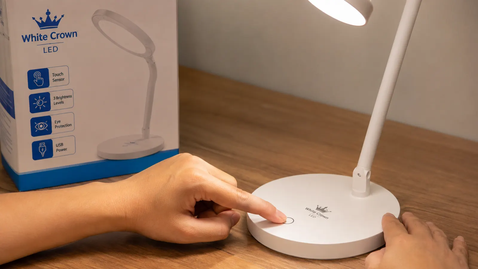 Hand pressing the touch-control button on the base of a White Crown LED desk lamp to cycle brightness